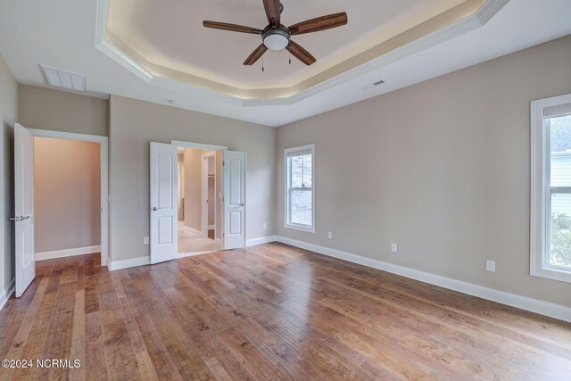 8711 Compass Pointe W Wynd Wynd NE, Leland, NC 28451 - unfurnished bedroom with visible vents, wood finished floors, a tray ceiling, and multiple windows
