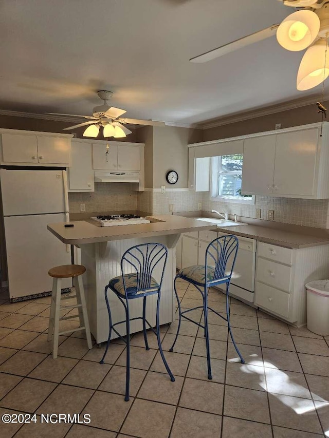 kitchen featuring white cabinets, a kitchen breakfast bar, ornamental molding, and white appliances