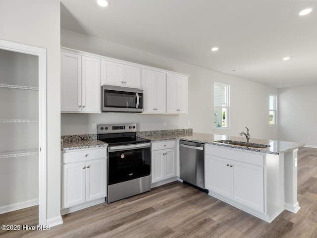 kitchen with white cabinets, light stone counters, appliances with stainless steel finishes, a peninsula, and a sink