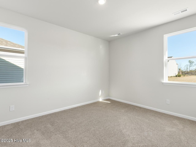 empty room with carpet floors, a healthy amount of sunlight, visible vents, and baseboards