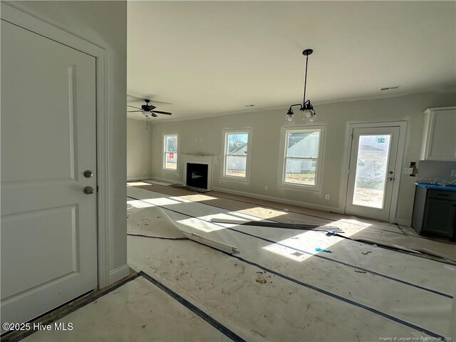 unfurnished living room featuring ceiling fan with notable chandelier and plenty of natural light