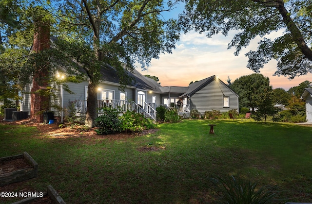 property exterior at dusk with cooling unit, a wooden deck, and a lawn