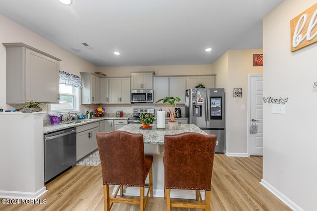 kitchen with gray cabinetry, appliances with stainless steel finishes, light hardwood / wood-style floors, and a center island