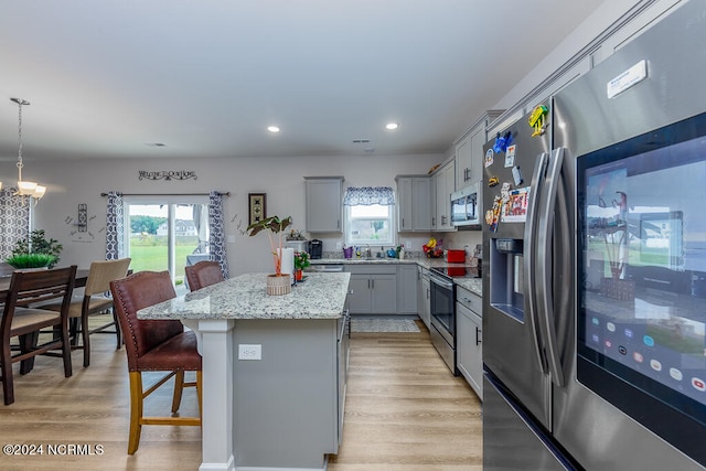 kitchen featuring hanging light fixtures, gray cabinetry, stainless steel appliances, a center island, and light hardwood / wood-style floors