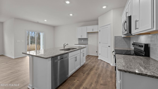 kitchen with a sink, stone counters, appliances with stainless steel finishes, and wood finished floors