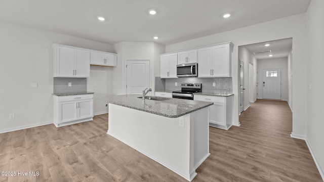 kitchen with light stone countertops, appliances with stainless steel finishes, an island with sink, and white cabinets