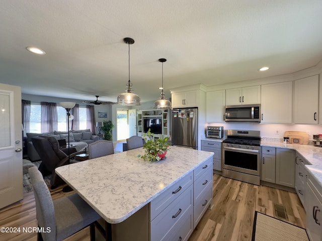 kitchen featuring a breakfast bar, appliances with stainless steel finishes, a center island, light hardwood / wood-style floors, and decorative light fixtures