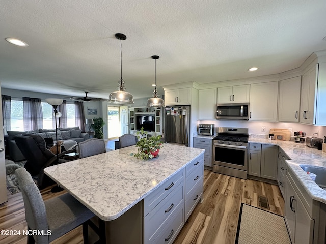 kitchen featuring light hardwood / wood-style flooring, hanging light fixtures, stainless steel appliances, a kitchen breakfast bar, and a kitchen island