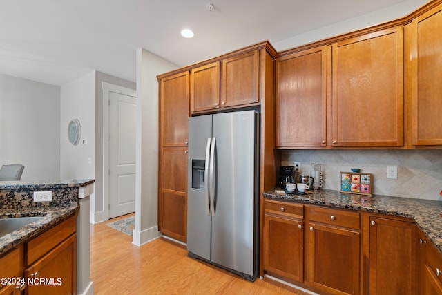 kitchen with light wood-type flooring, stainless steel fridge, dark stone counters, and tasteful backsplash