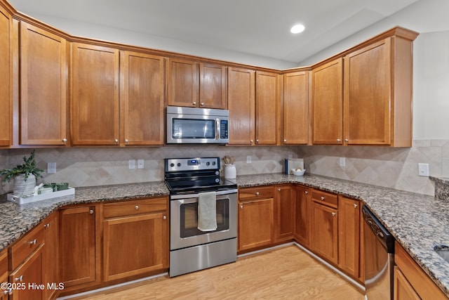 2537 St James Dr SE Unit 303, Southport, NC 28461 - kitchen with appliances with stainless steel finishes, light wood-type flooring, stone countertops, decorative backsplash, and brown cabinets
