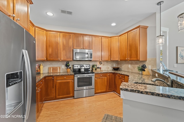 kitchen featuring dark stone countertops, stainless steel appliances, hanging light fixtures, and light hardwood / wood-style flooring