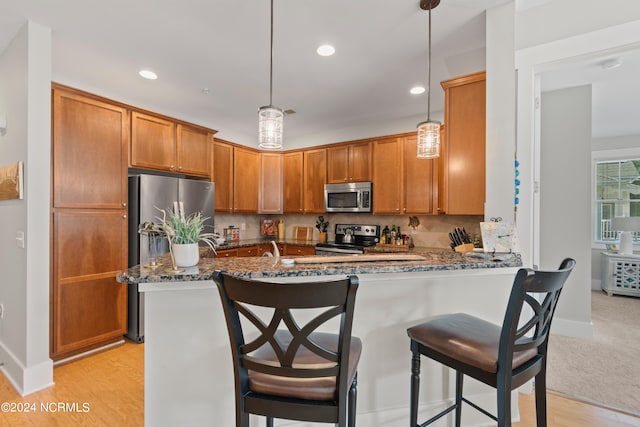 kitchen with light wood-type flooring, kitchen peninsula, stainless steel appliances, decorative light fixtures, and dark stone countertops