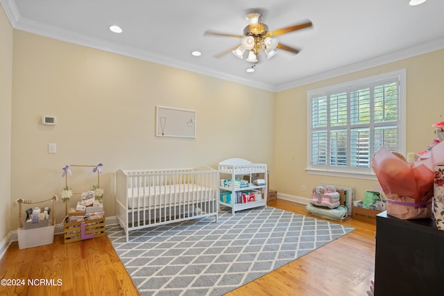 bedroom with wood-type flooring, a nursery area, crown molding, and ceiling fan