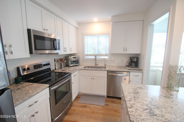 kitchen with white cabinets, light stone countertops, sink, appliances with stainless steel finishes, and light wood-type flooring