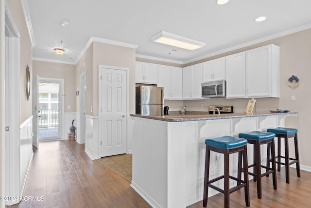 kitchen featuring appliances with stainless steel finishes, white cabinets, kitchen peninsula, crown molding, and light hardwood / wood-style flooring