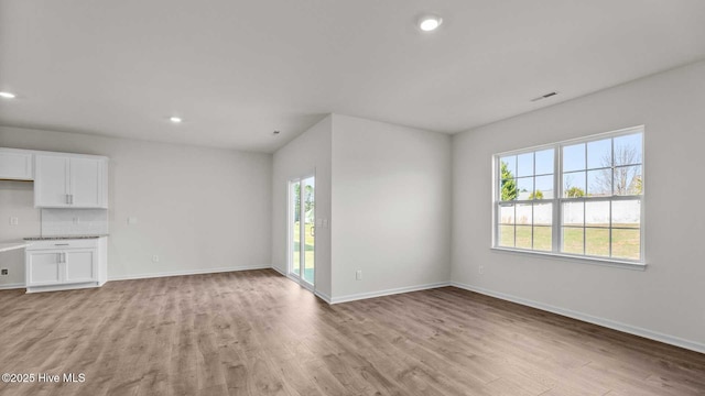 unfurnished living room with light wood-type flooring, visible vents, and baseboards