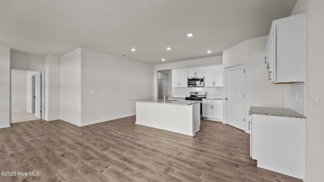 kitchen featuring a sink, stainless steel microwave, light stone counters, backsplash, and wood finished floors