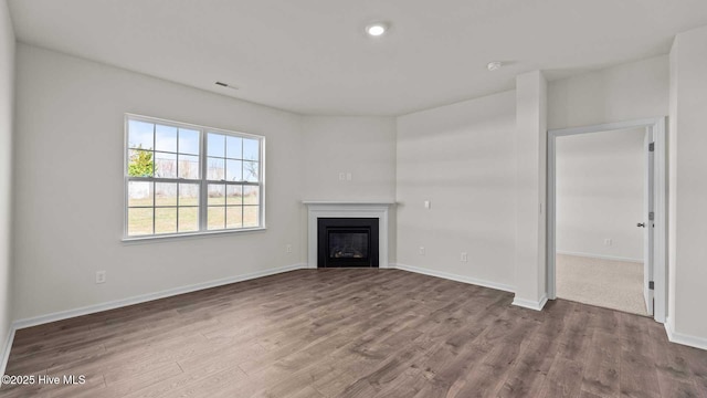 unfurnished living room with a glass covered fireplace, visible vents, baseboards, and wood finished floors