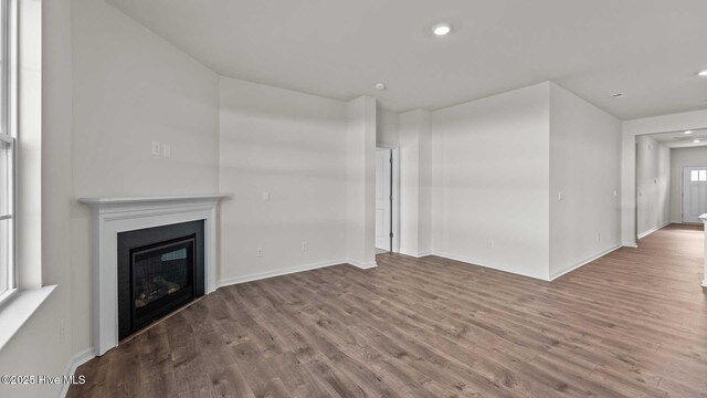 unfurnished living room featuring a glass covered fireplace, recessed lighting, wood finished floors, and baseboards