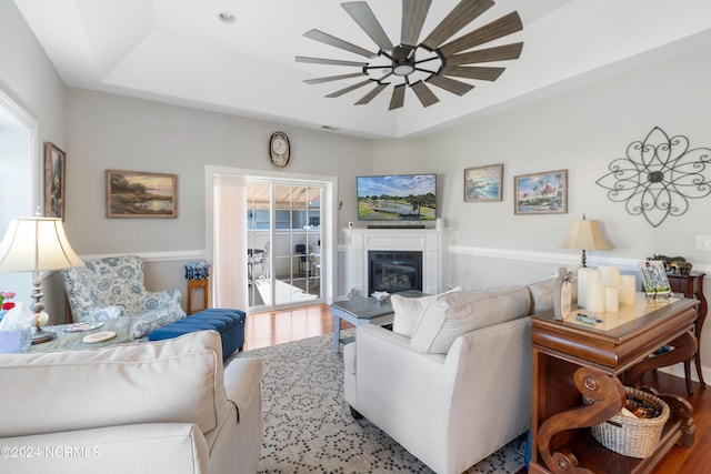 living room with ceiling fan, a wealth of natural light, a tray ceiling, and hardwood / wood-style floors