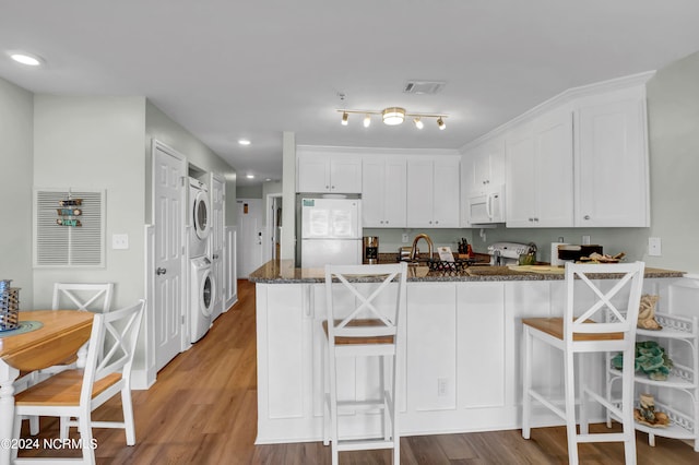 kitchen with white appliances, stacked washer / dryer, white cabinetry, a kitchen breakfast bar, and light hardwood / wood-style floors