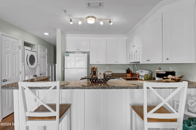 kitchen with stacked washer and clothes dryer, a kitchen breakfast bar, white cabinets, and white appliances