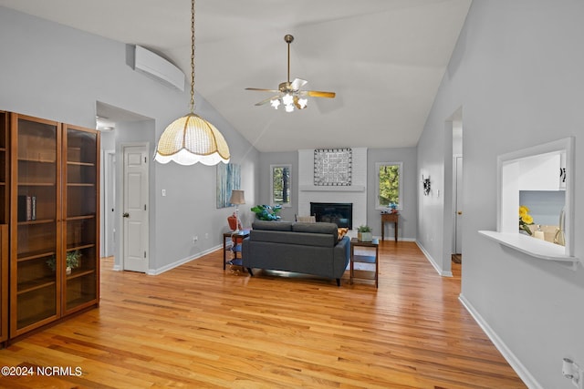 living room featuring high vaulted ceiling, a brick fireplace, light hardwood / wood-style flooring, ceiling fan, and a wall mounted AC