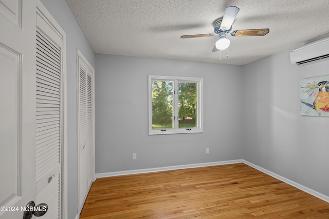 unfurnished bedroom featuring an AC wall unit, ceiling fan, a textured ceiling, and light wood-type flooring