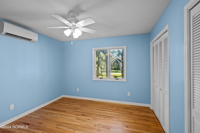 unfurnished bedroom with a wall mounted air conditioner, a textured ceiling, ceiling fan, light hardwood / wood-style floors, and a closet