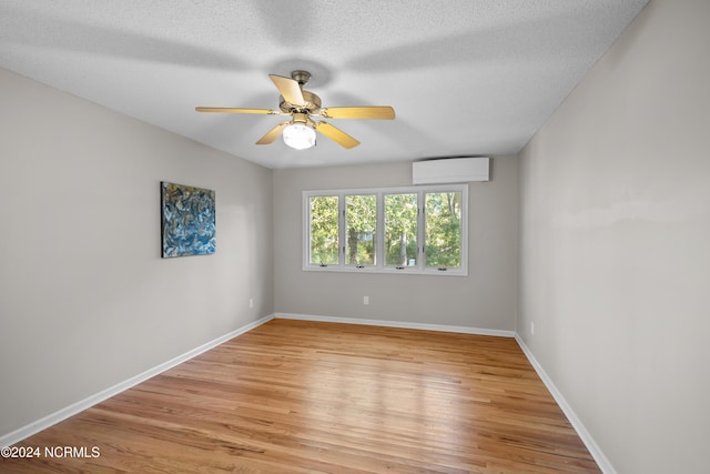 unfurnished room featuring a textured ceiling, ceiling fan, light hardwood / wood-style flooring, and a wall mounted air conditioner