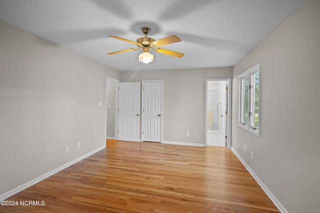 unfurnished bedroom with a textured ceiling, ceiling fan, light hardwood / wood-style flooring, and ensuite bath