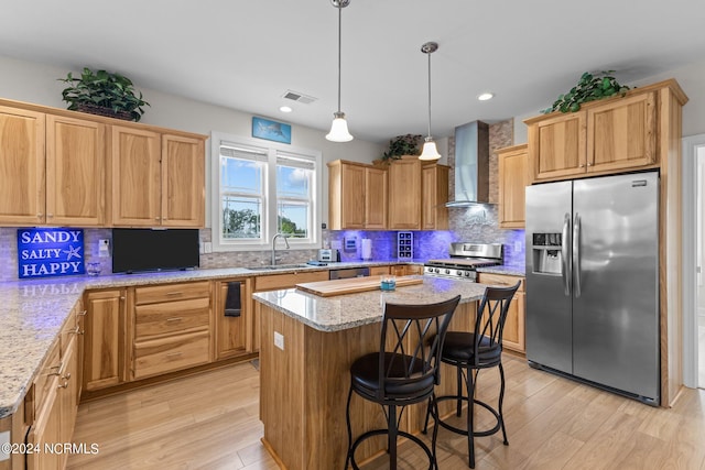 kitchen with light hardwood / wood-style floors, a kitchen island, wall chimney range hood, decorative backsplash, and stainless steel appliances