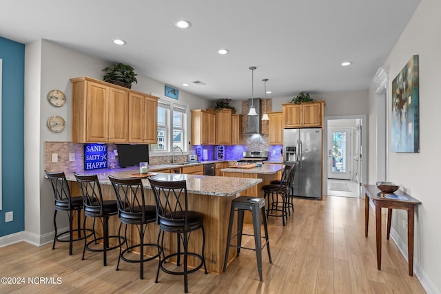 kitchen featuring a breakfast bar area, wall chimney exhaust hood, light hardwood / wood-style flooring, appliances with stainless steel finishes, and decorative light fixtures