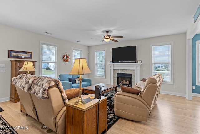 living room with light wood-type flooring, ceiling fan, a tile fireplace, and plenty of natural light