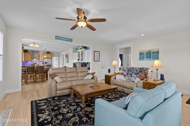 living room with light wood-type flooring, ceiling fan with notable chandelier, and plenty of natural light