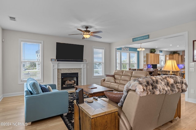 living room with ceiling fan with notable chandelier, light hardwood / wood-style flooring, a tile fireplace, and a wealth of natural light