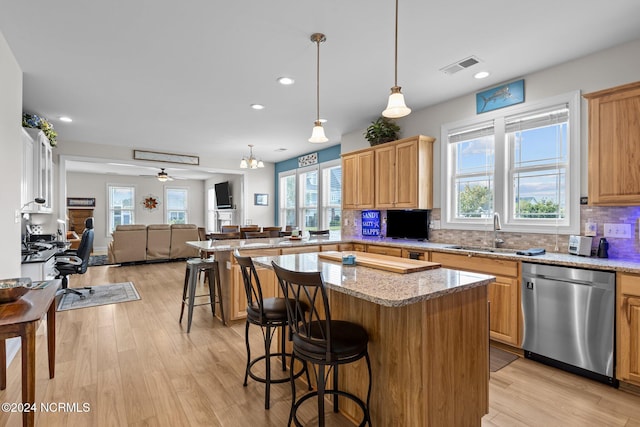 kitchen with light hardwood / wood-style floors, stainless steel dishwasher, a breakfast bar, and plenty of natural light