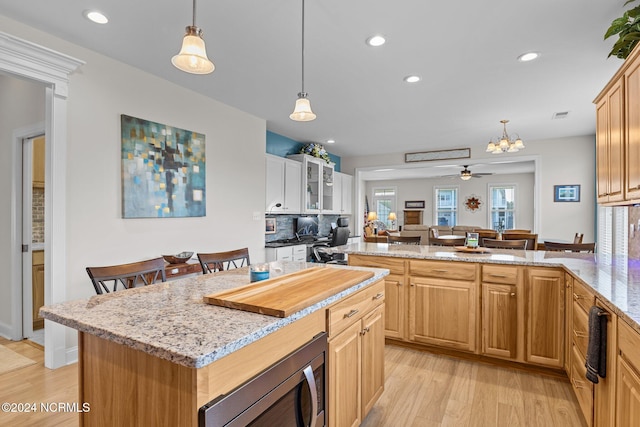 kitchen with ceiling fan, kitchen peninsula, backsplash, light wood-type flooring, and stainless steel microwave