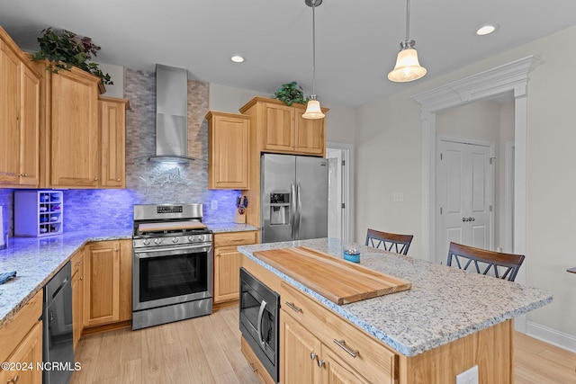 kitchen with a center island, hanging light fixtures, wall chimney range hood, light hardwood / wood-style flooring, and black appliances