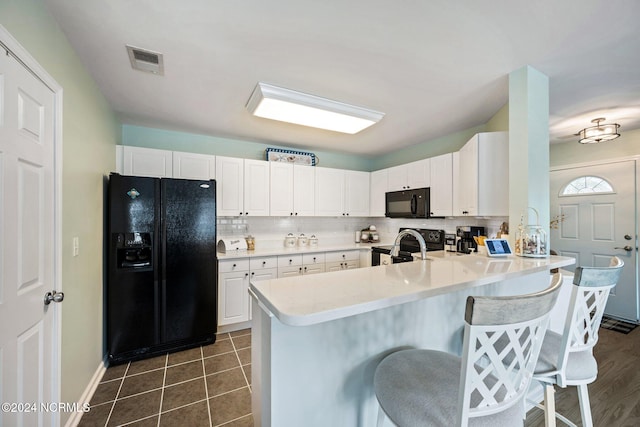 kitchen with white cabinets, kitchen peninsula, backsplash, black appliances, and a breakfast bar area