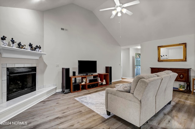 living room featuring hardwood / wood-style flooring, high vaulted ceiling, ceiling fan, and a tile fireplace