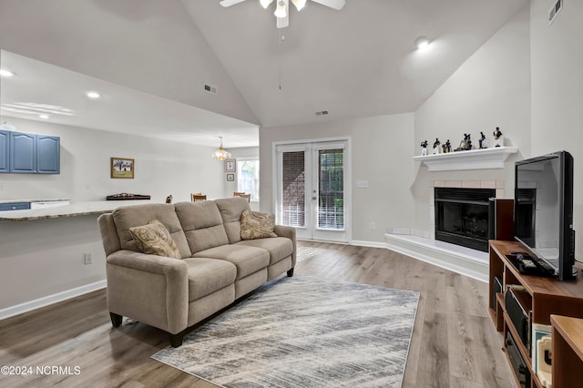 living room featuring ceiling fan, high vaulted ceiling, a tiled fireplace, and light hardwood / wood-style flooring