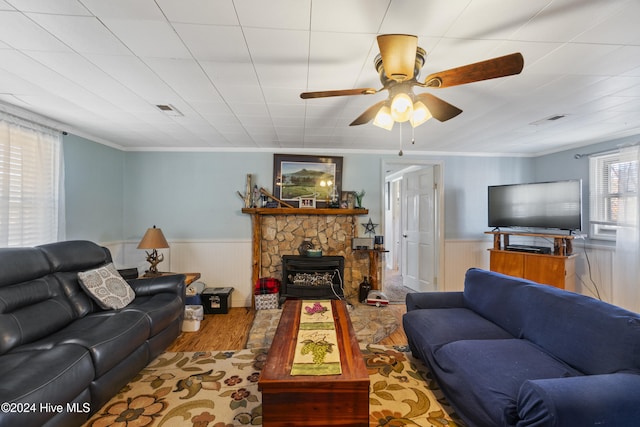 living room with light hardwood / wood-style floors, a wood stove, ceiling fan, and ornamental molding