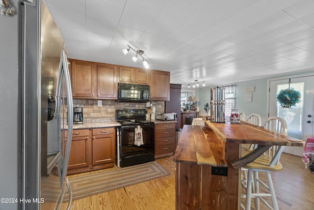 kitchen featuring decorative backsplash, light hardwood / wood-style floors, a healthy amount of sunlight, and black appliances