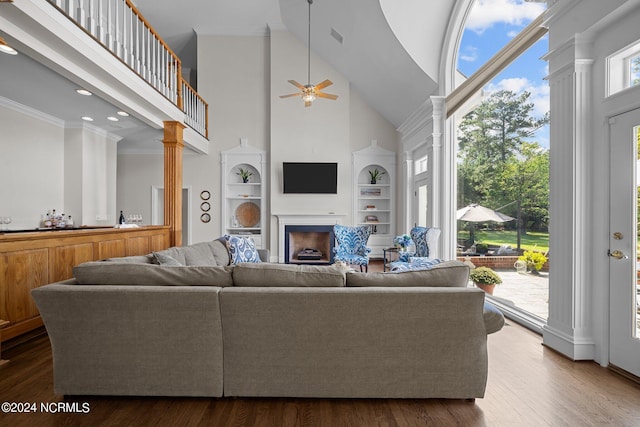 living room with wood-type flooring, crown molding, a high ceiling, ceiling fan, and ornate columns