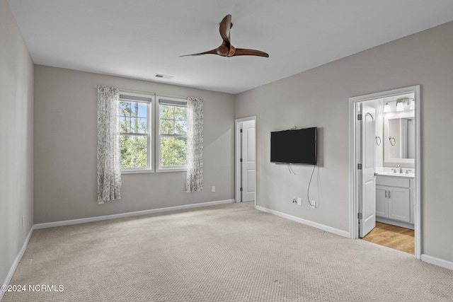 unfurnished bedroom featuring light carpet, ensuite bath, ceiling fan, and sink