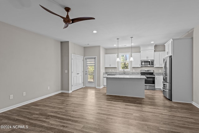 kitchen with appliances with stainless steel finishes, ceiling fan, decorative light fixtures, white cabinets, and a kitchen island