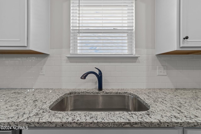 interior details featuring white cabinetry, light stone countertops, sink, and decorative backsplash