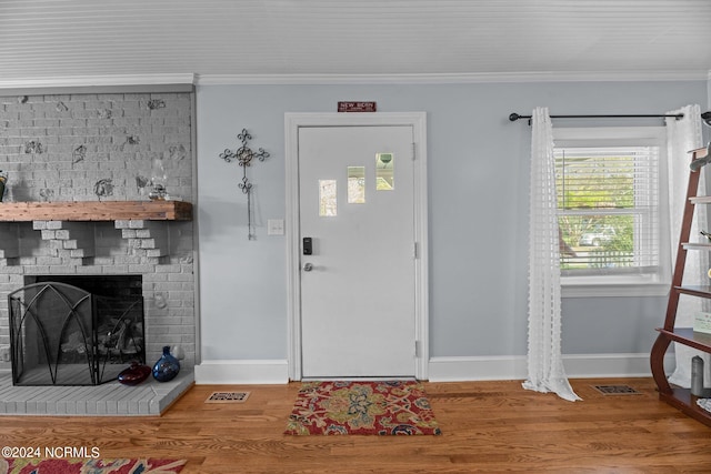 foyer entrance featuring wood-type flooring, a brick fireplace, and crown molding