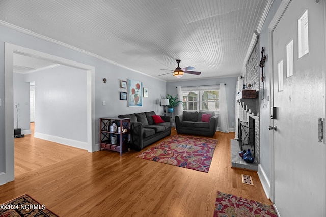 living room featuring ornamental molding, hardwood / wood-style floors, ceiling fan, and a brick fireplace